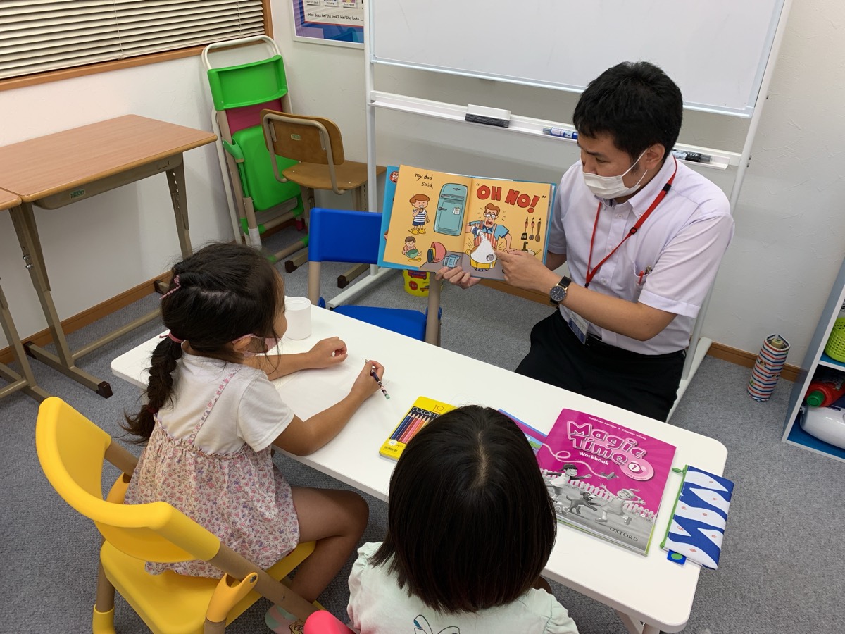 講師が絵本を見せながら、机を囲む子どもたちにレッスンをしている様子
