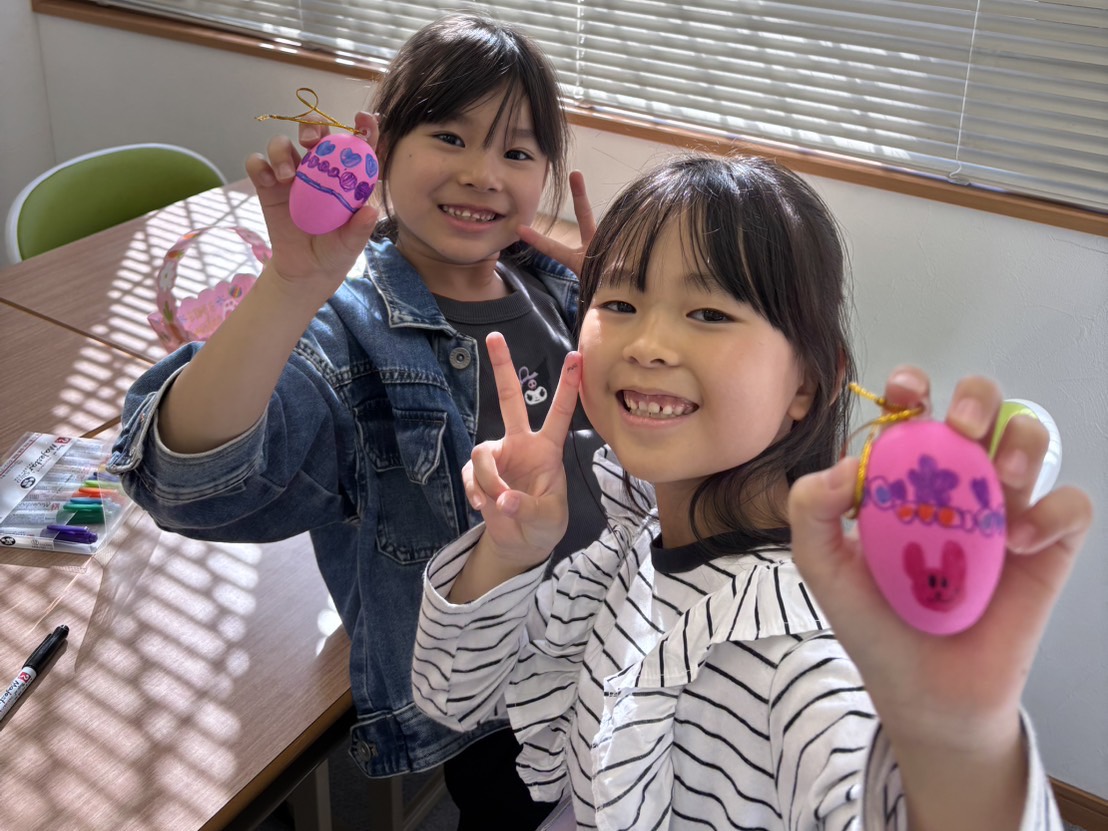 手作りのイースターエッグを見せる、笑顔の女の子2人