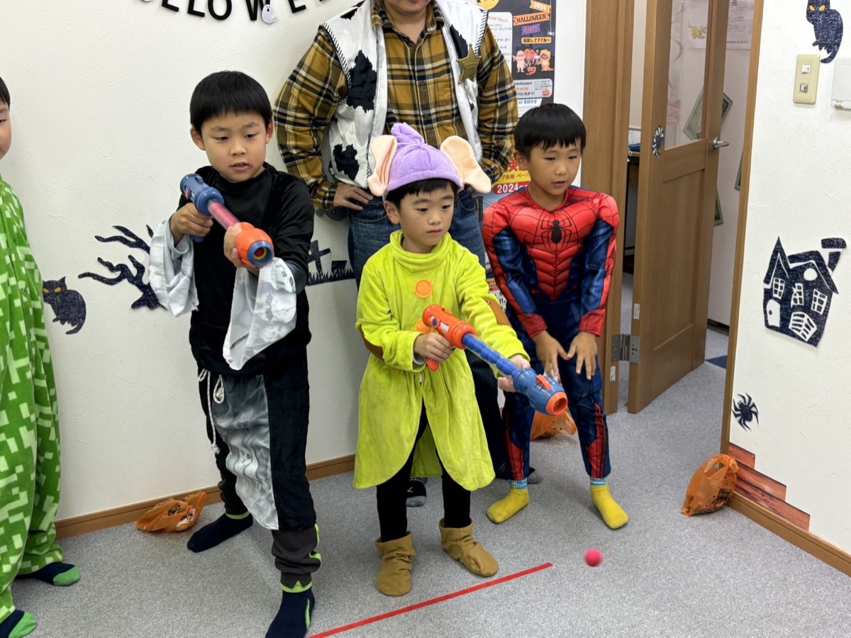 ハロウィンの仮装をして、おもちゃのボール当てゲームをする子どもたち