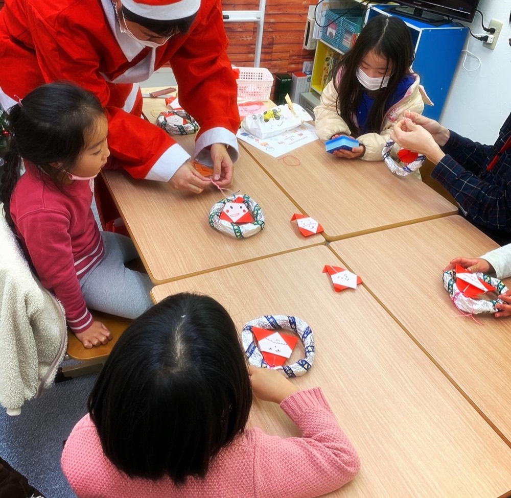 サンタクロースの衣装の講師と、折り紙のサンタでリースを作る子どもたち