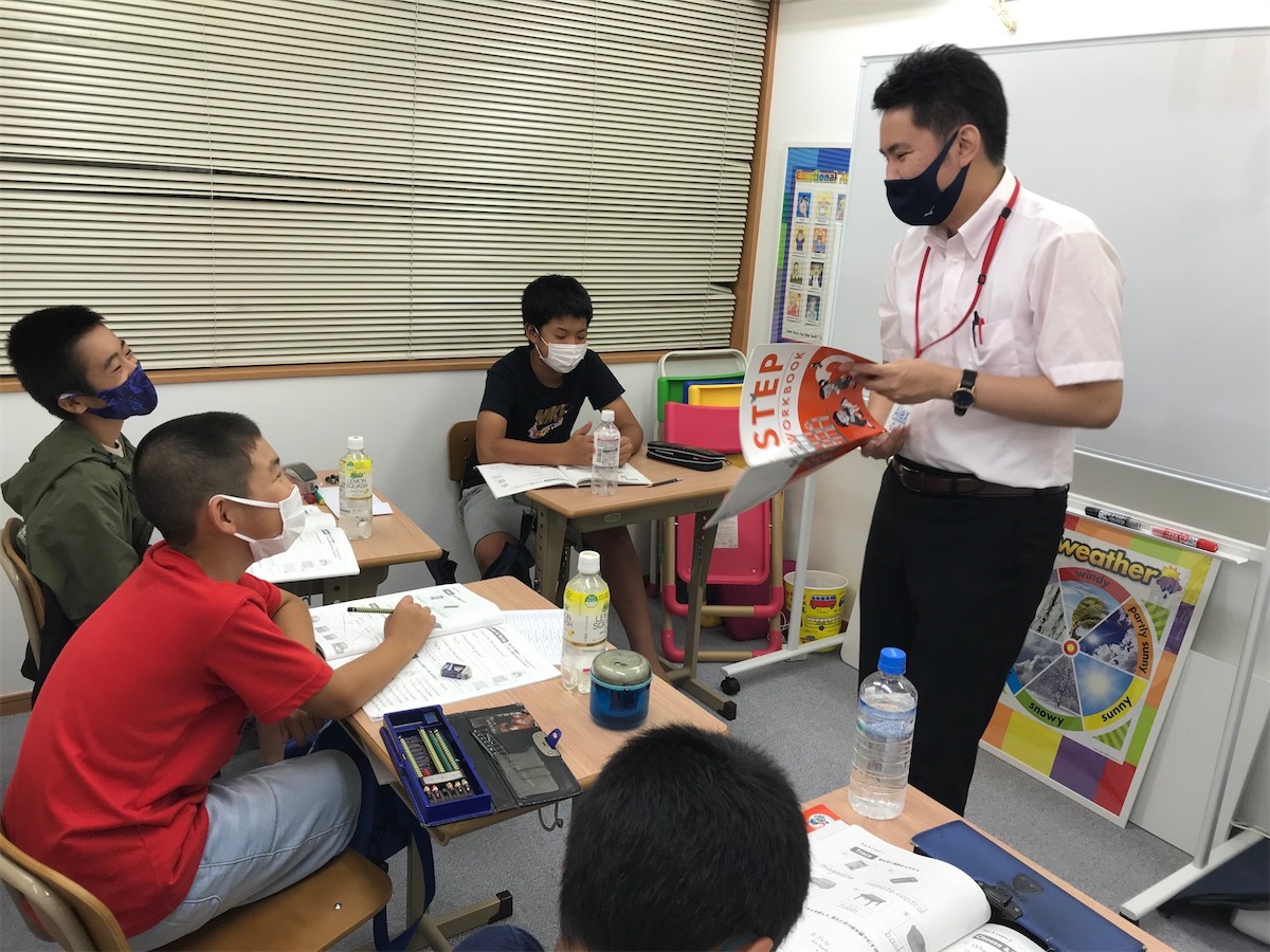 アレックス先生がテキストを見せながら、子どもたちにレッスンをしている様子
