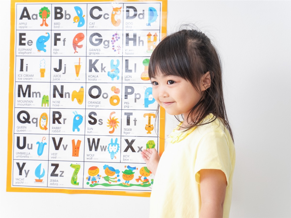 アルファベット表の前で、にっこり笑う女の子
